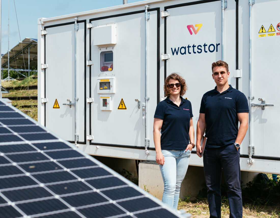 Two Wattstor team members, Veronika and Filip, standing in front of a Wattstor battery storage container at the TON solar site.
