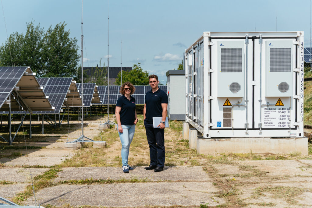 Two Wattstor team members, Veronika and Filip, standing in front of a Wattstor battery storage container at the TON solar site.