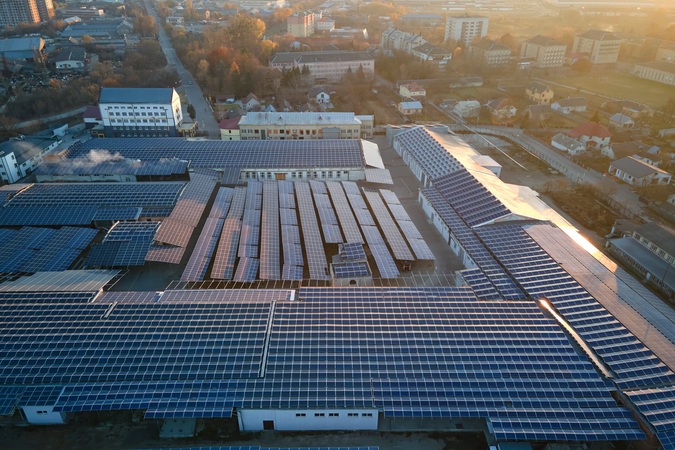 Aerial view of solar power plant with blue photovoltaic panels mounted on industrial building roof for producing green ecological electricity. Production of sustainable energy concept